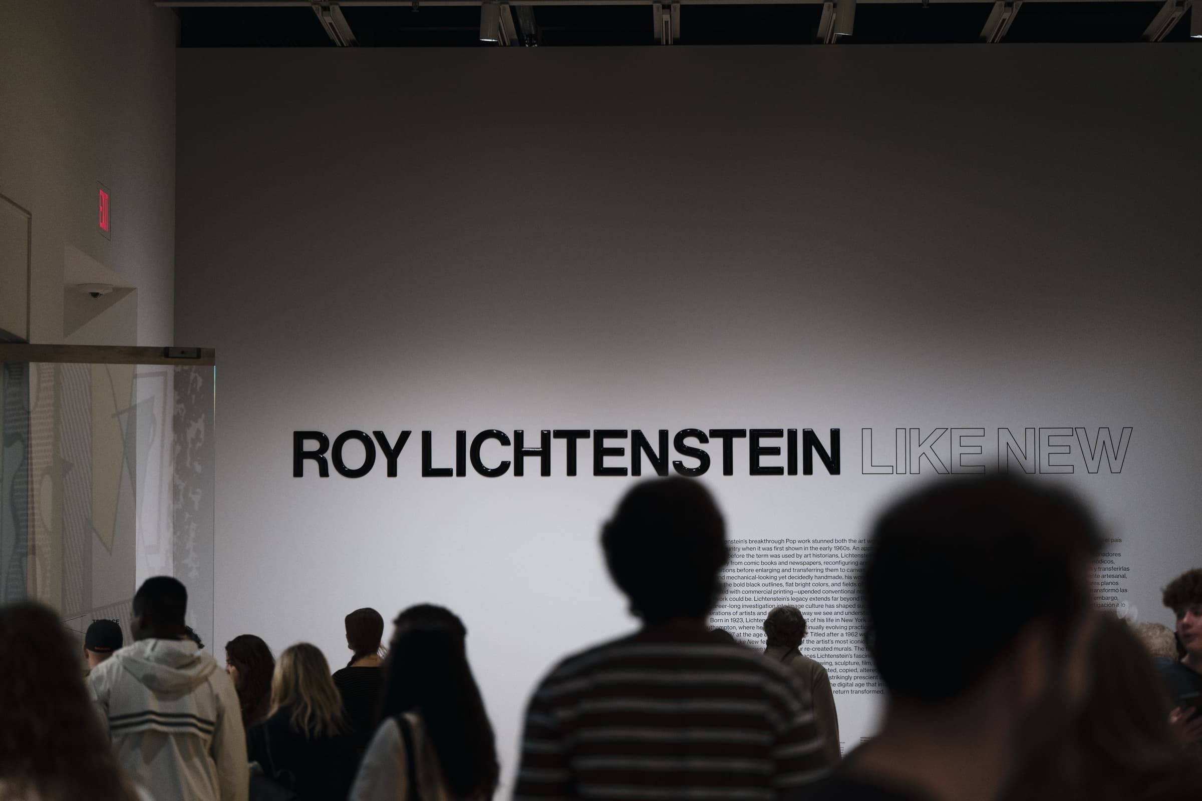 白い壁に「ROY LICHTENSTEIN LIKE NEW」の文字。手前を来場者が歩く