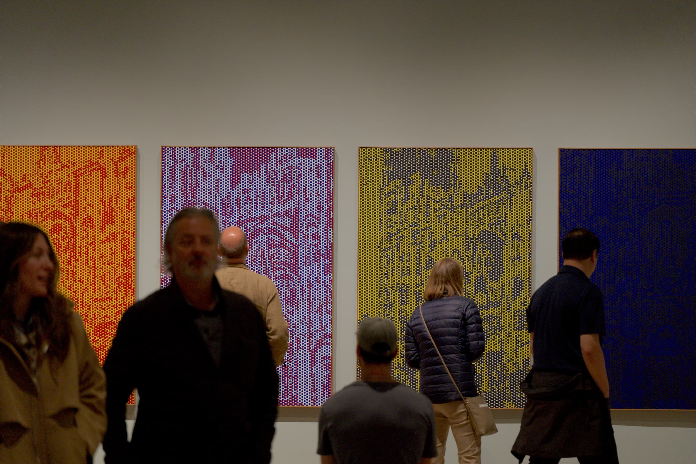 Tall paintings in yellow, pink and blue dots hang side by side as visitors stand in front