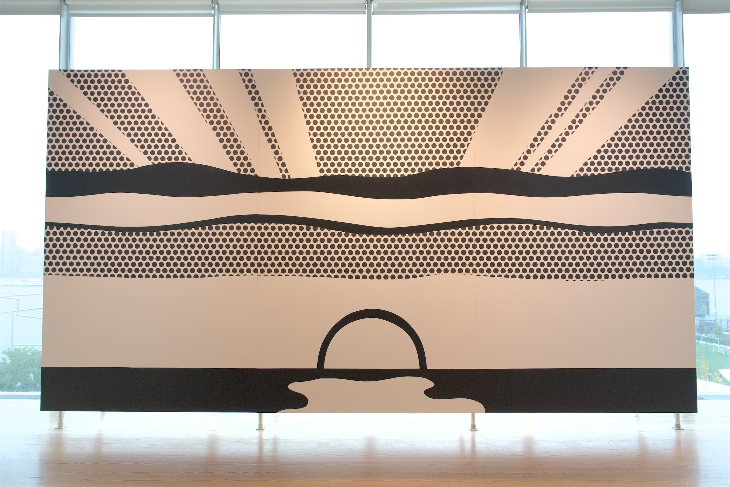 A long black-and-white panel of a sun and waves in dots, set before the gallery windows