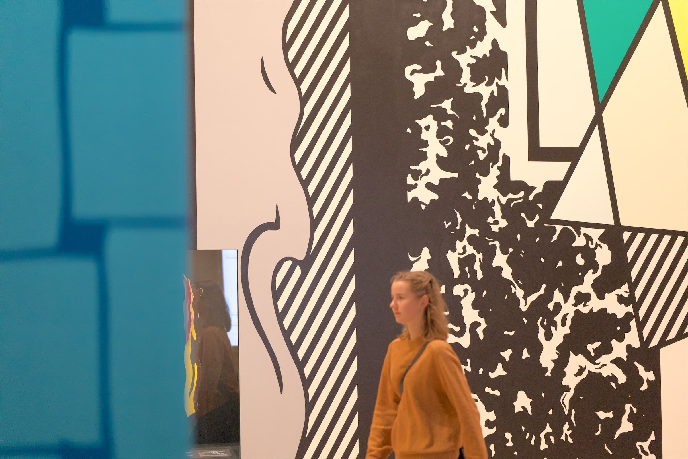 A visitor walks in front of a mural of black-and-white patterns and teal panels