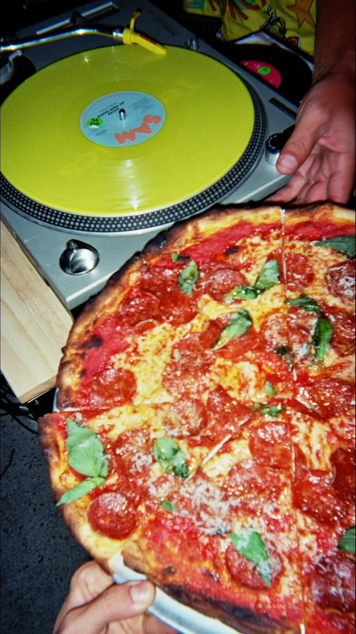 A thin-crust pizza next to a turntable at Balera