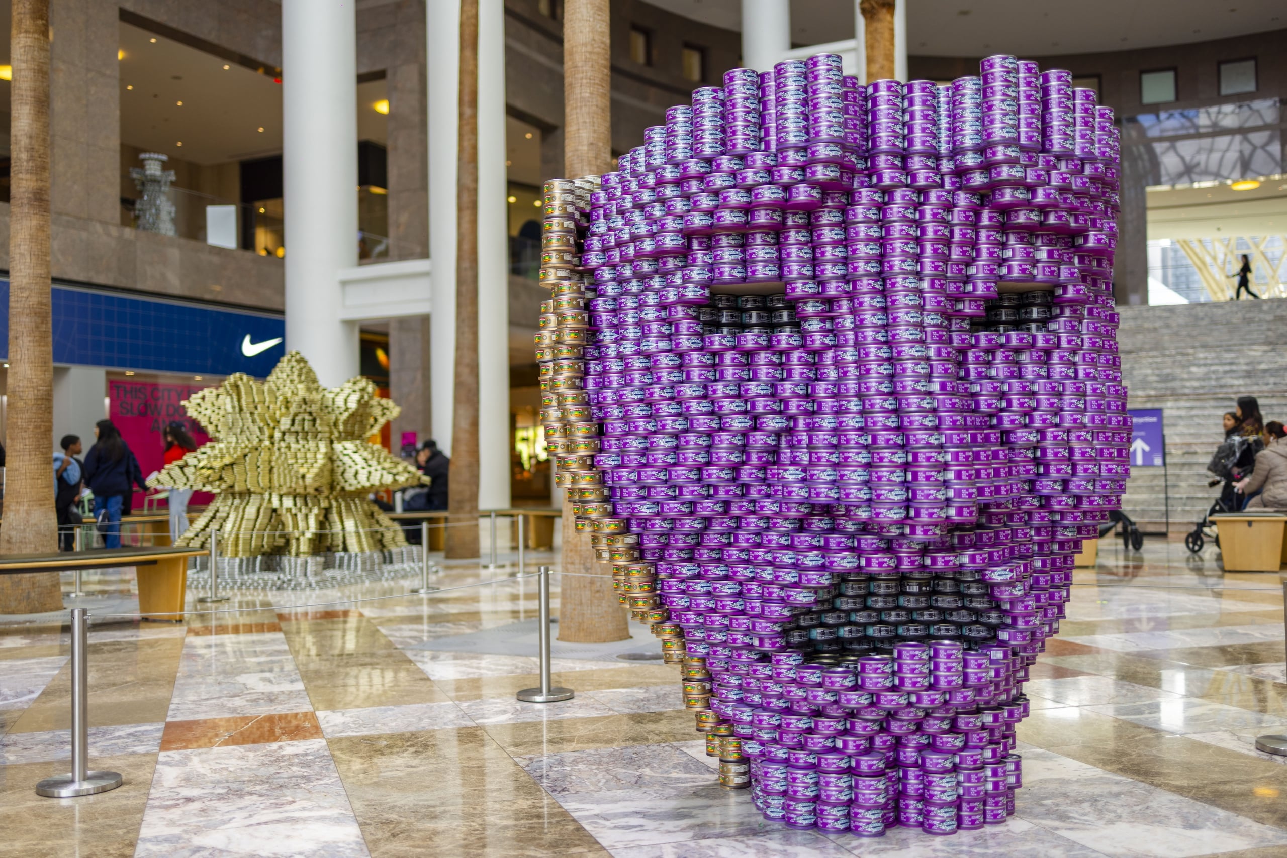 Purple tuna-can face sculpture with a gold can sculpture behind it