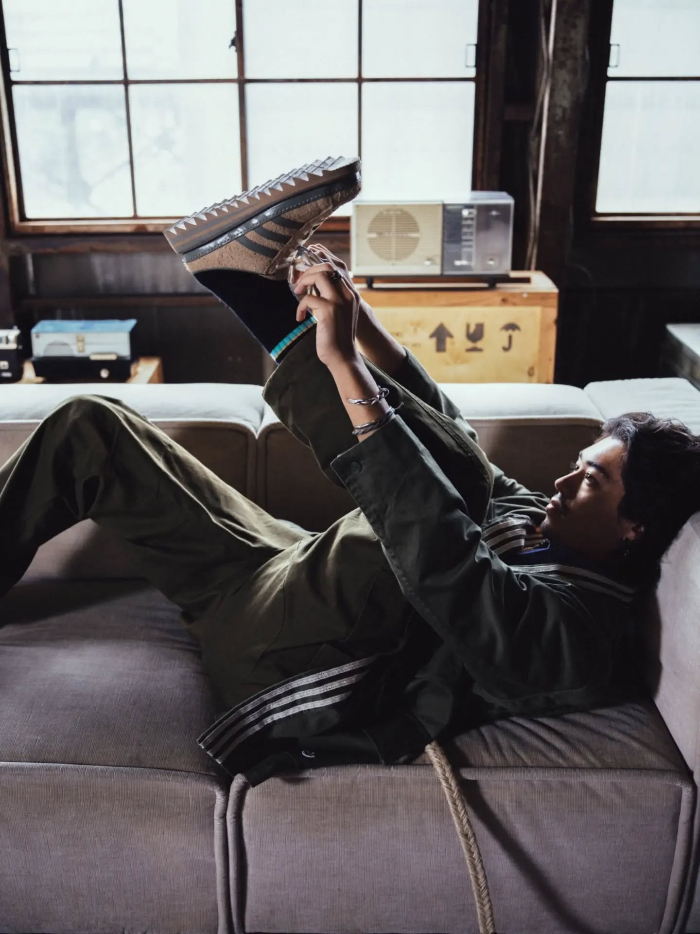 Model lying on a sofa holding up the tan CLOT x adidas Superstar mule with sawtooth sole