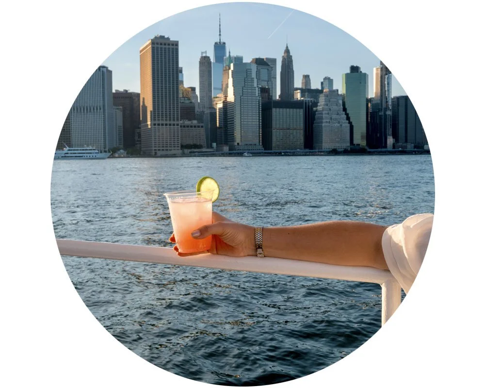 Cocktail held on the railing with the Manhattan skyline across the water
