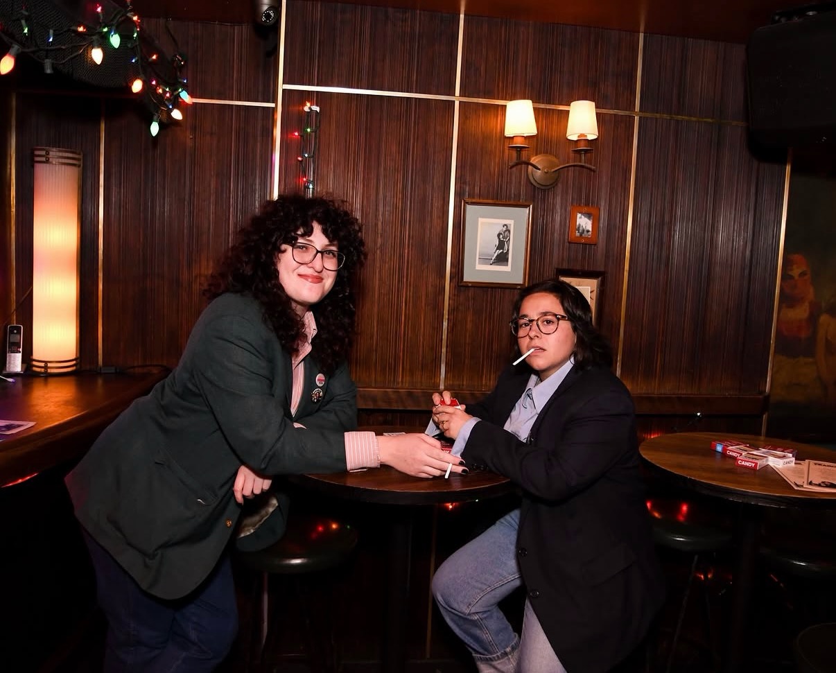 Two guests posing with candy cigarettes at a wood-paneled table