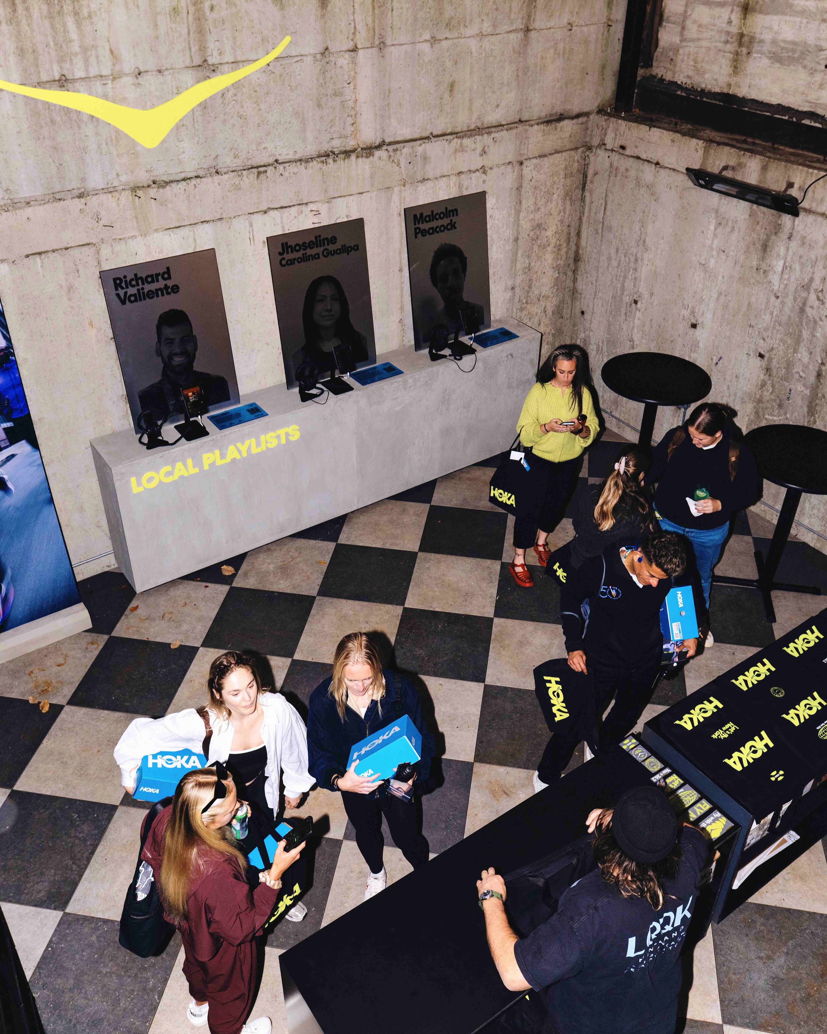 Visitors with HOKA shoe boxes and tote bags beside the Local Playlists listening station