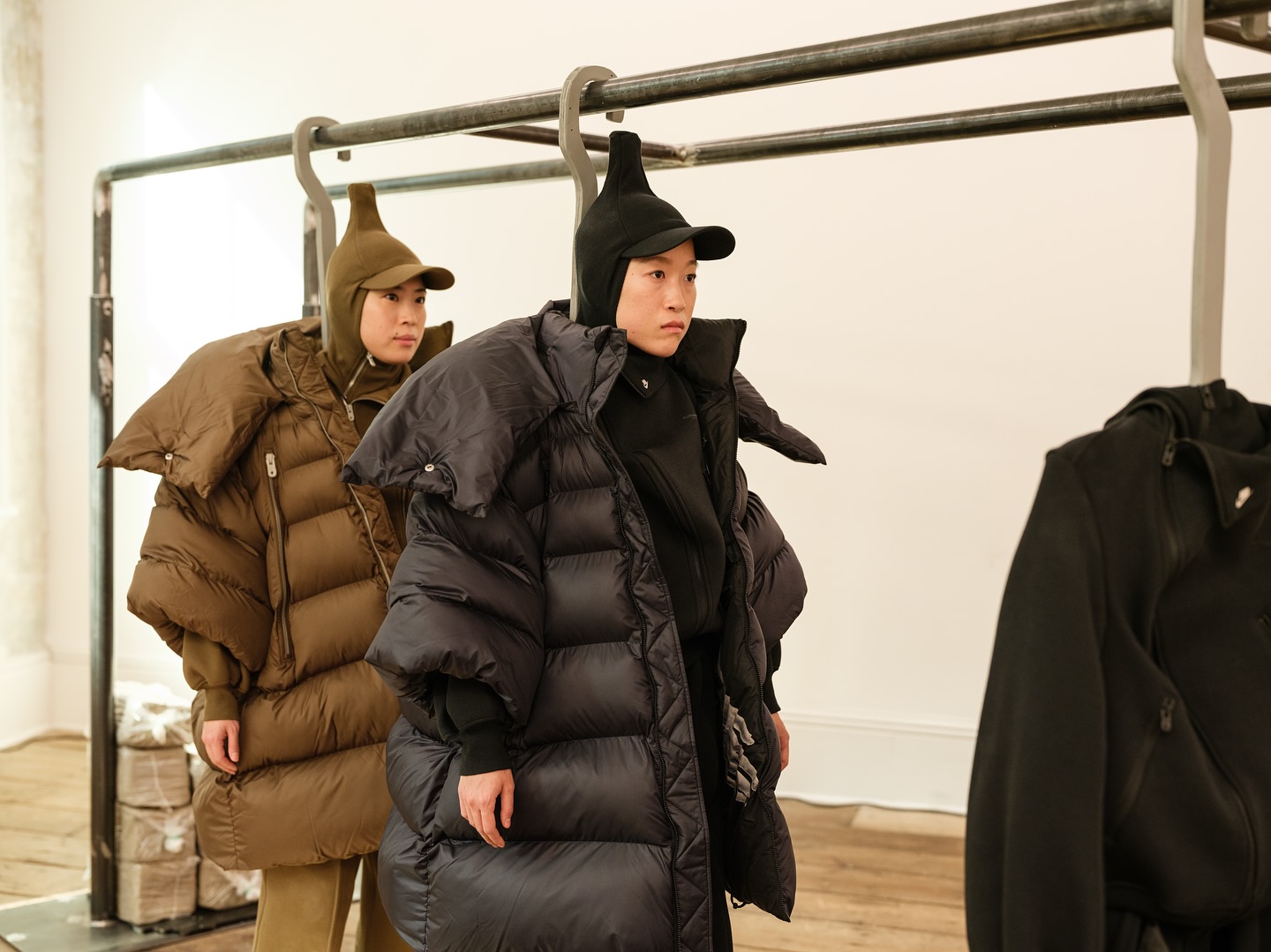 Models in oversized brown and black puffer coats beside a clothing rack