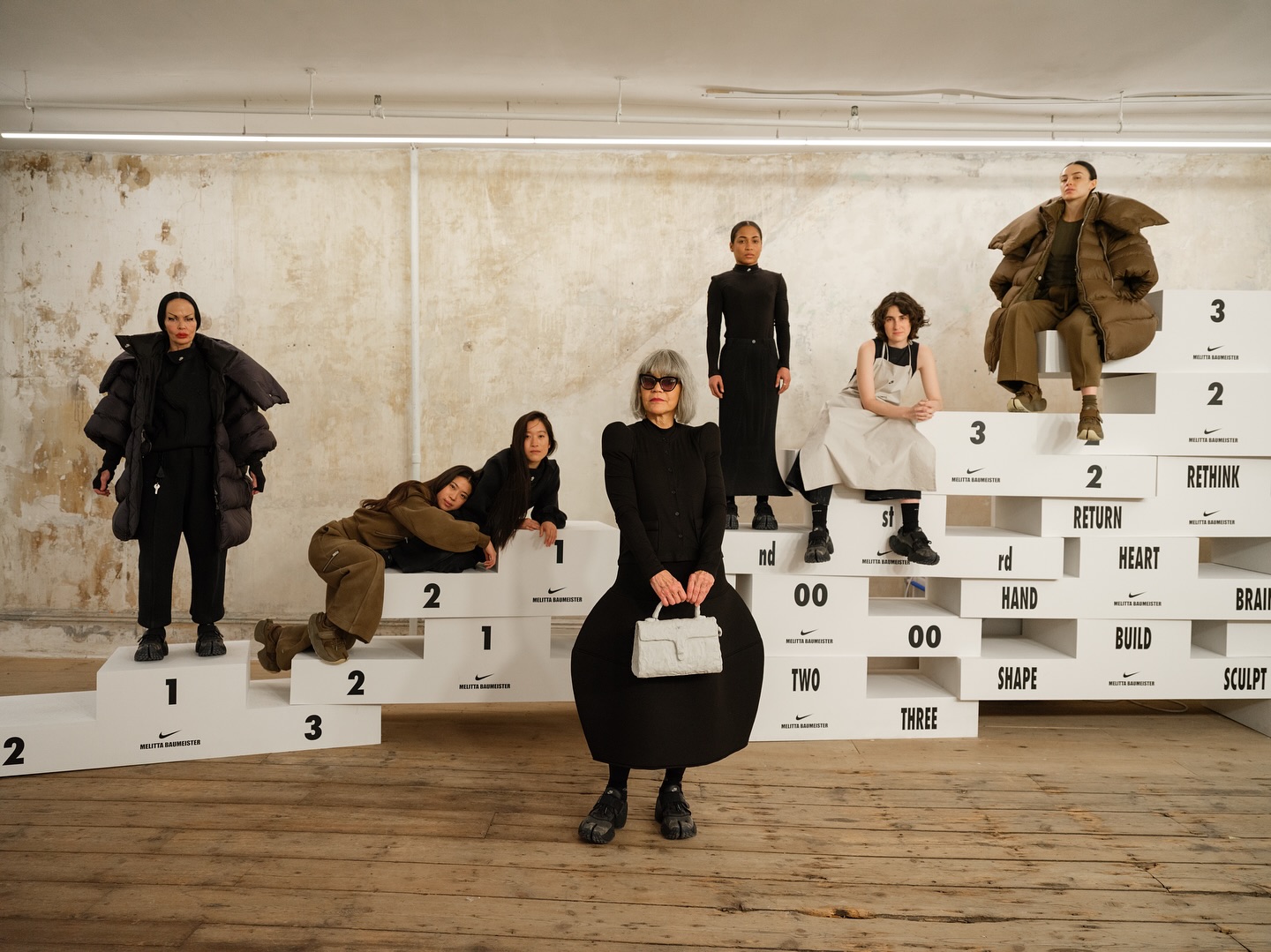 Cast posed on white podium-style platforms in a loft