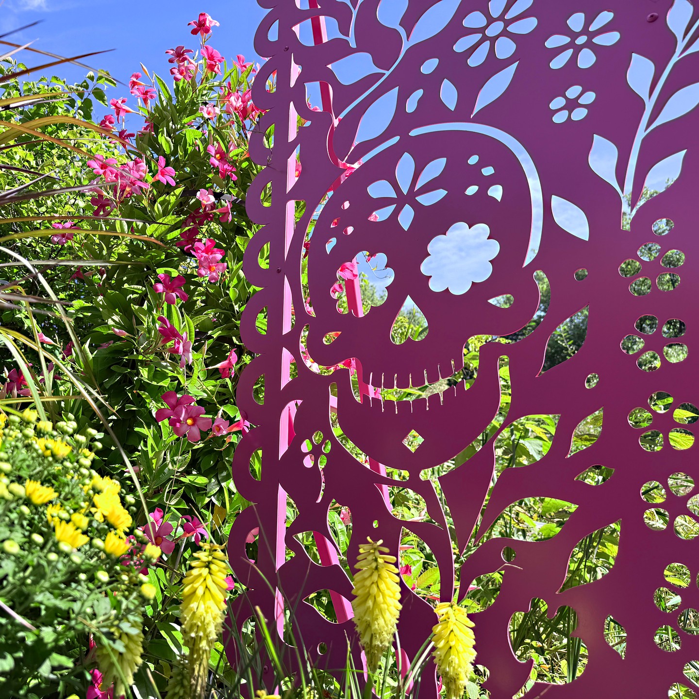Pink cut-metal skull panel among flowers at NYBG's Día de los Muertos trail