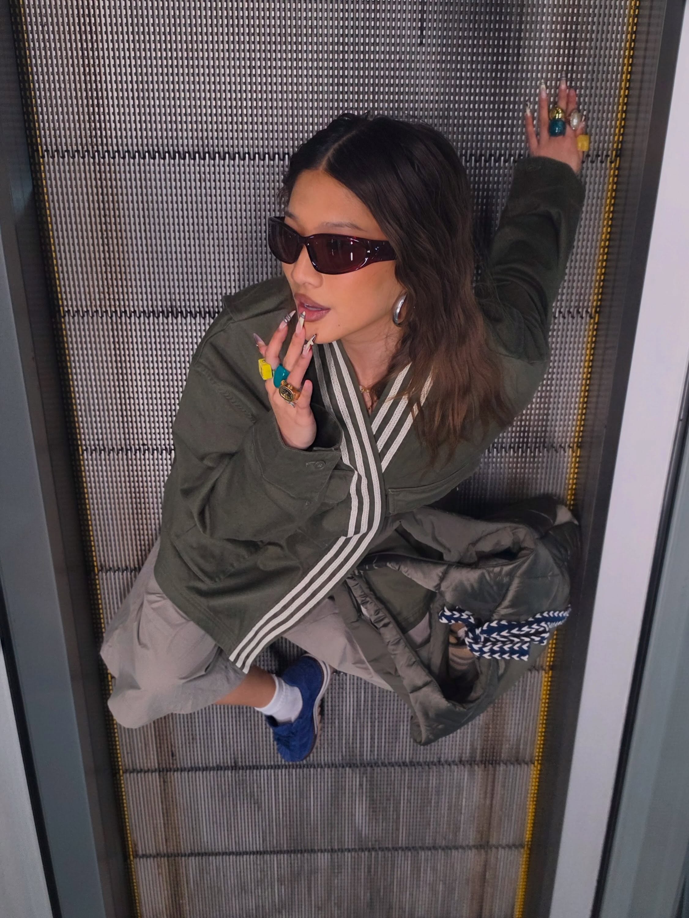 Model in an olive three-stripe CLOT x adidas jacket on an escalator